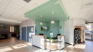 A modern reception area with a teal wall, wooden reception desk, and a large potted plant.