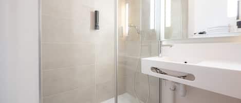 Ein modernes Badezimmer mit einer in Glas eingefassten Dusche, einem weißen Waschbecken und einem Spiegel darüber.