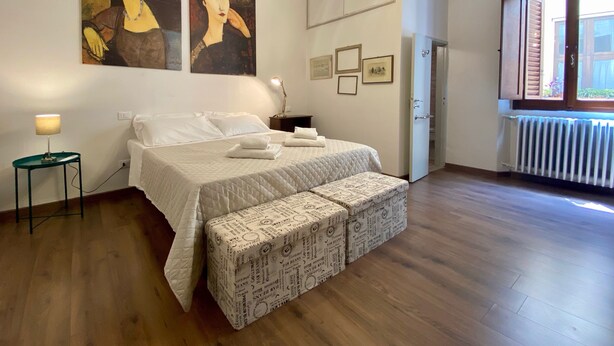 A bedroom with a bed, bedside lamp, artwork, air conditioning unit, and a view of the outside. - Pinzochere - Two Bedroom Apartment, Sleeps 4 (Firenze)