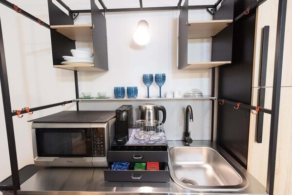 Cocina compacta con microondas, cafetera y lavabo.