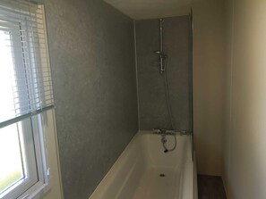 A bathroom with a bathtub, a shower, and a window with blinds. - Lodge - Sleeps 8 - Parking, Wifi, (Clacton-on-Sea)