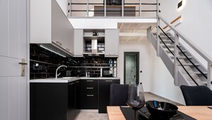 Eine moderne Küche mit schwarzen Schränken, ein Essbereich mit einem Holztisch und eine Treppe, die zu einer oberen Ebene führt.