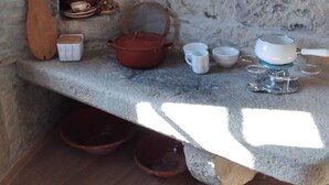 A stone-walled kitchen with a built-in oven, various kitchen utensils, and cookware.