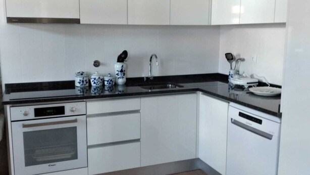 A modern kitchen with white cabinets, a black countertop, a built-in oven, and a dishwasher.