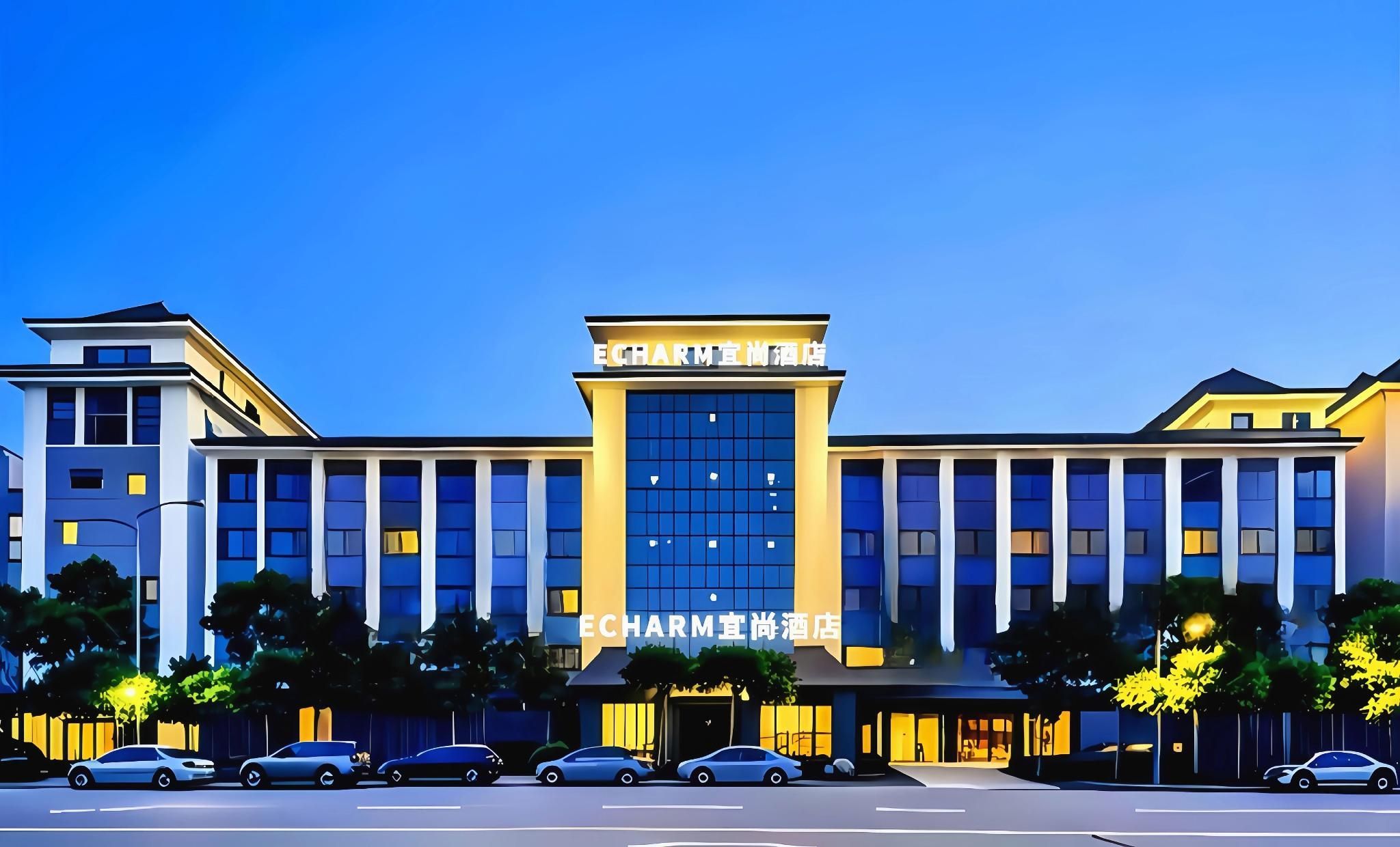 A modern hotel with a central entrance, multiple floors, and a parking area in front.