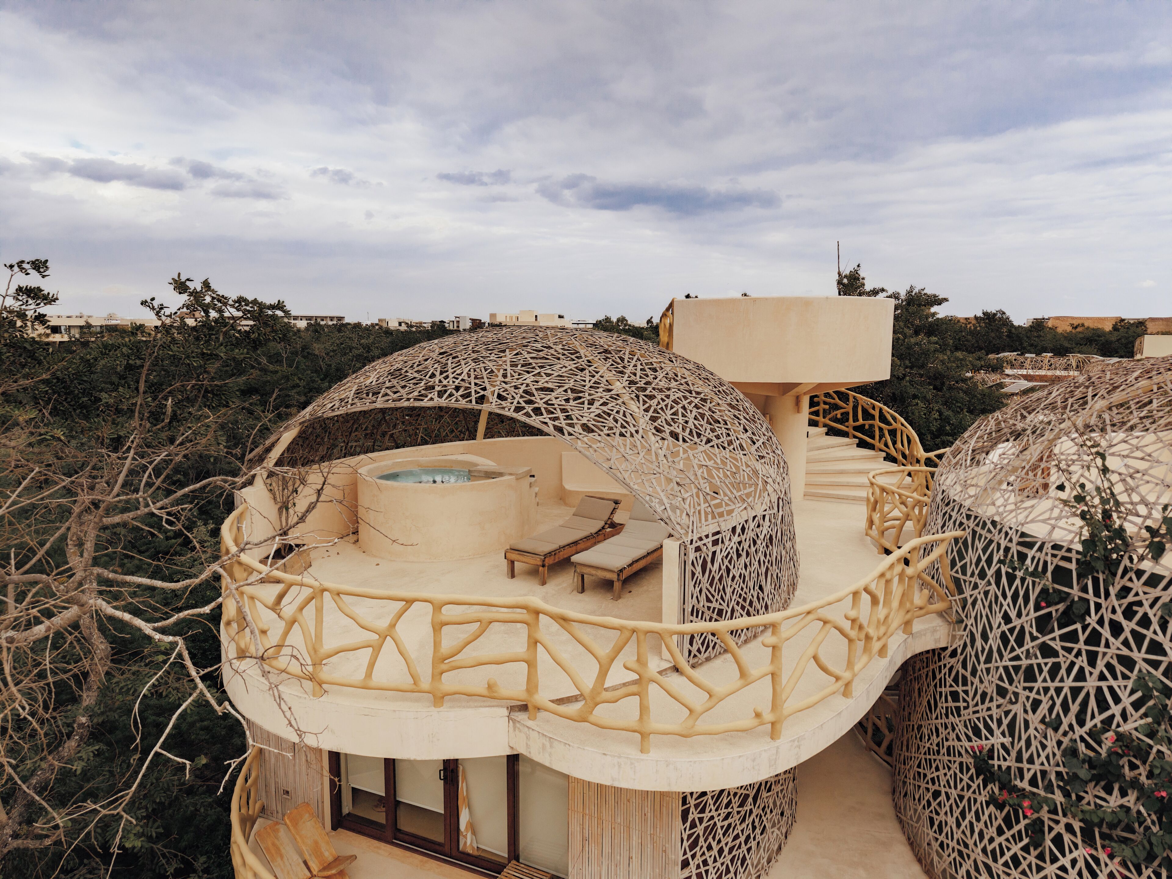 A modern, dome-shaped building with a hot tub and outdoor seating area, surrounded by natural vegetation.