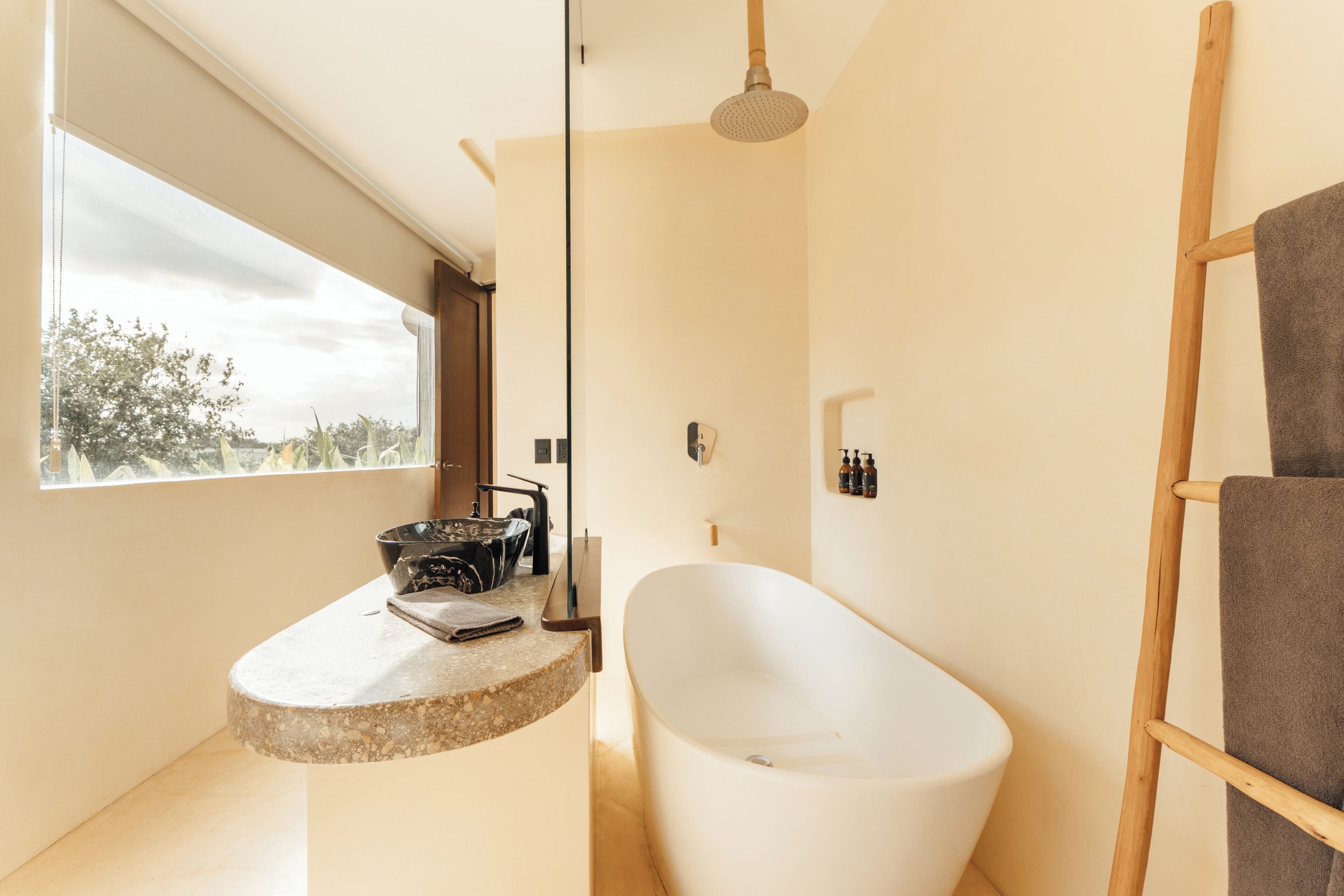A modern bathroom with a freestanding bathtub, a large window, and a wooden ladder.