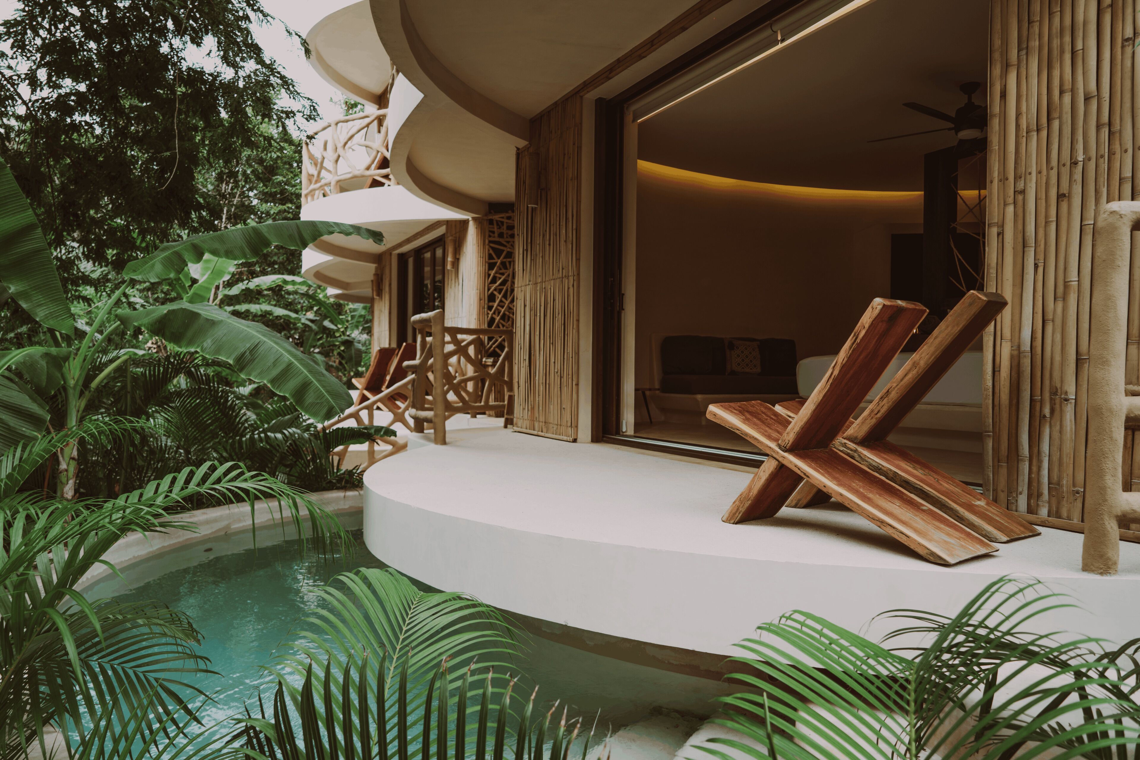A poolside area with a curved deck, wooden lounge chairs, and lush greenery.