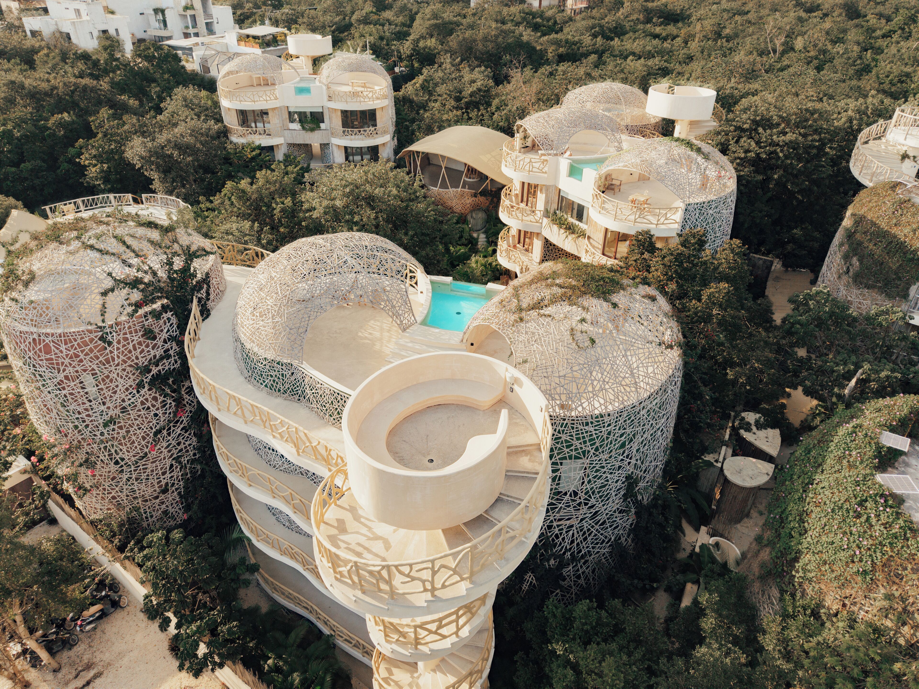 Ein modernes Resort mit mehreren kuppelförmigen Gebäuden, einem zentralen Pool und üppiger, das Anwesen umgebender Bepflanzung.
