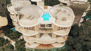 A multi-level, circular building with balconies, a central pool, and surrounding greenery.