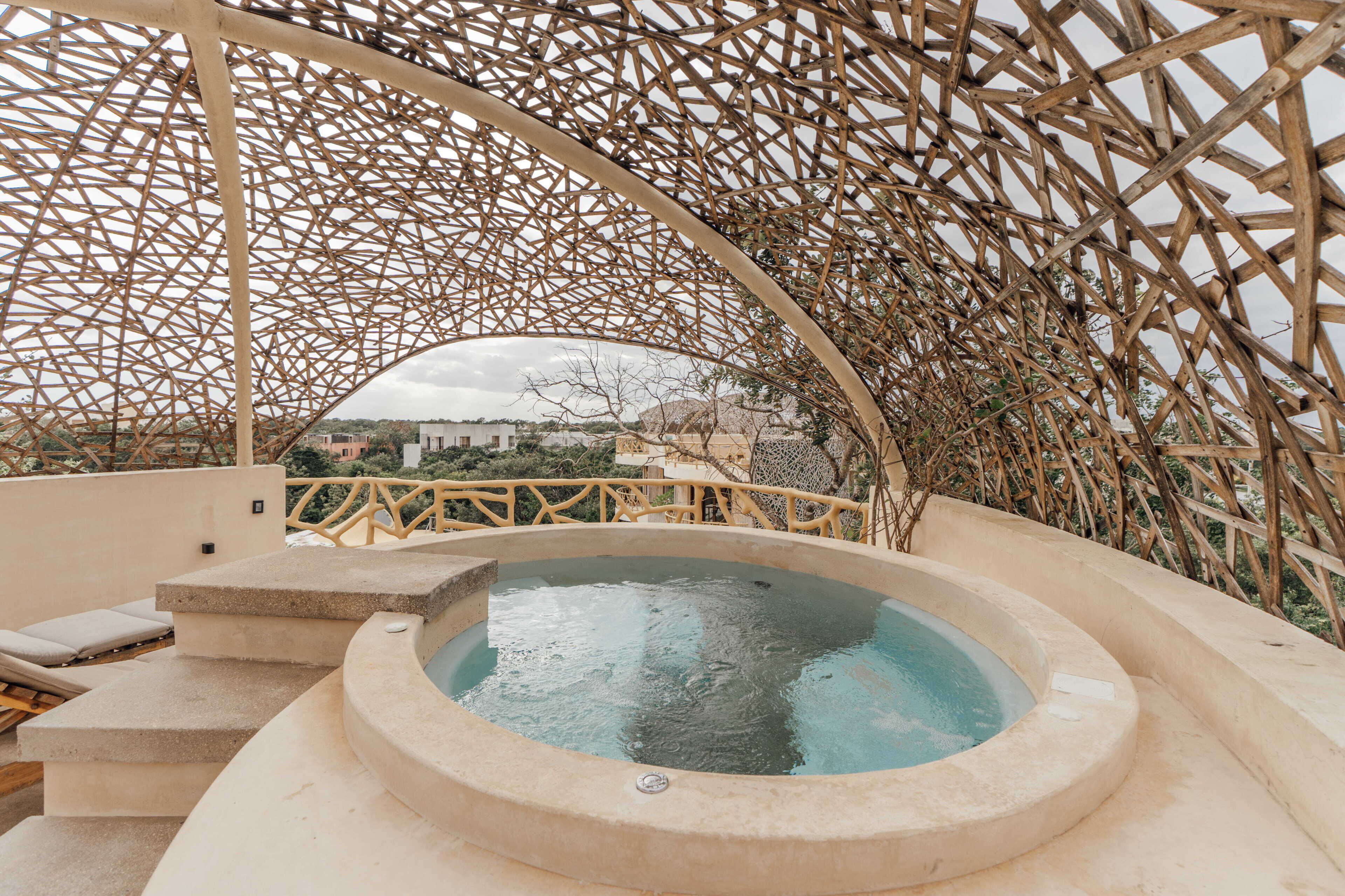 Un bain à remous installé sous une structure en treillis de bois, avec vue sur les bâtiments en arrière-plan.