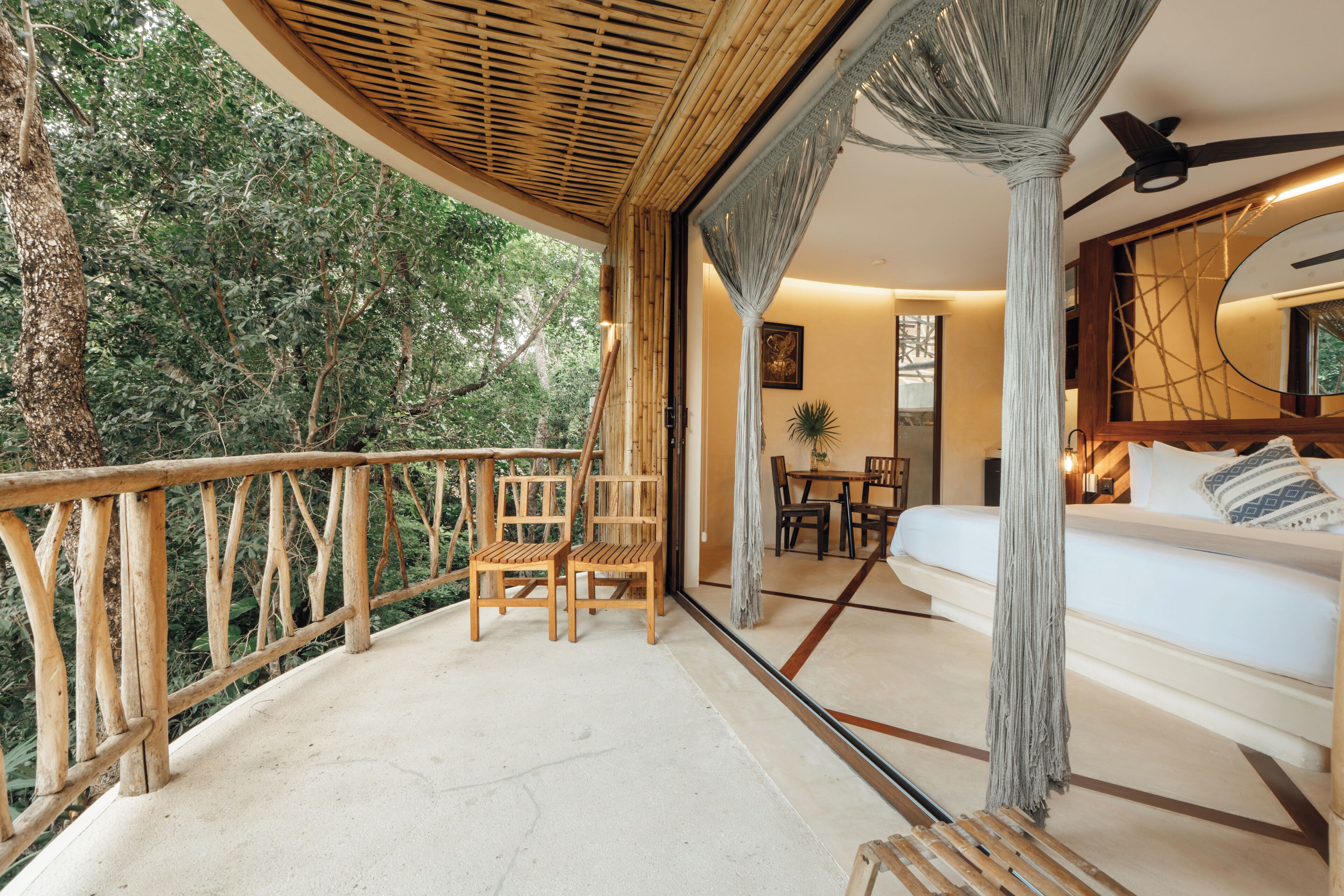 A balcony with wooden chairs and a table, overlooking a lush green forest.