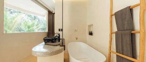 Ein modernes Badezimmer mit einer freistehenden Badewanne, einem hölzernen Handtuchhalter und einem Fenster mit Blick auf Grünflächen.