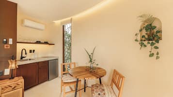 A compact kitchen with a dining area, featuring a round wooden table, two wooden chairs, a built-in oven, and a wall-mounted plant.