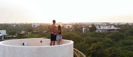 A couple standing on a circular observation deck with a railing, overlooking a cityscape and greenery.