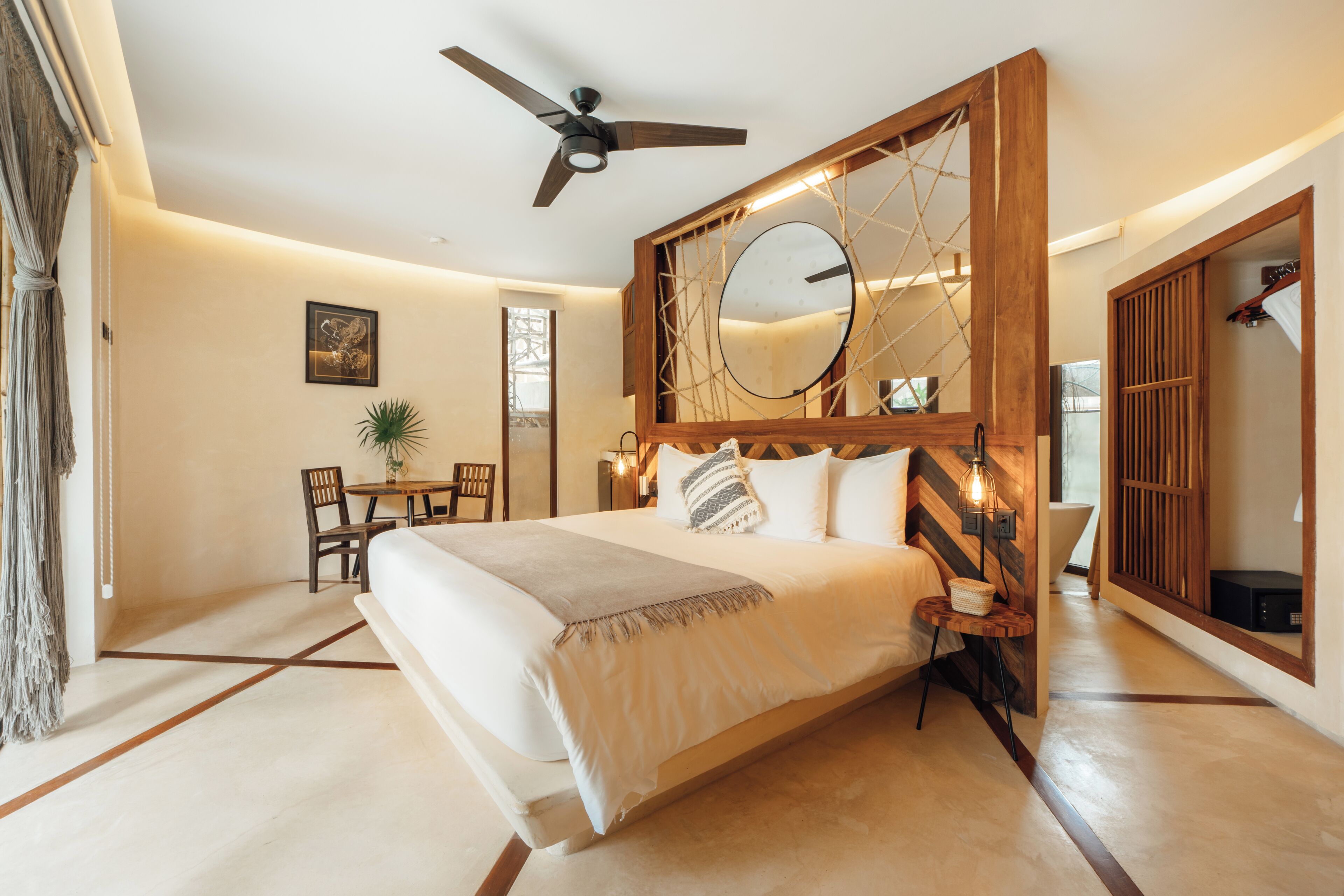 Ein modernes Schlafzimmer mit einem großen Bett, einem Deckenventilator, einem Holz-Kopfteil, einem Nachttisch und einem Spiegel.