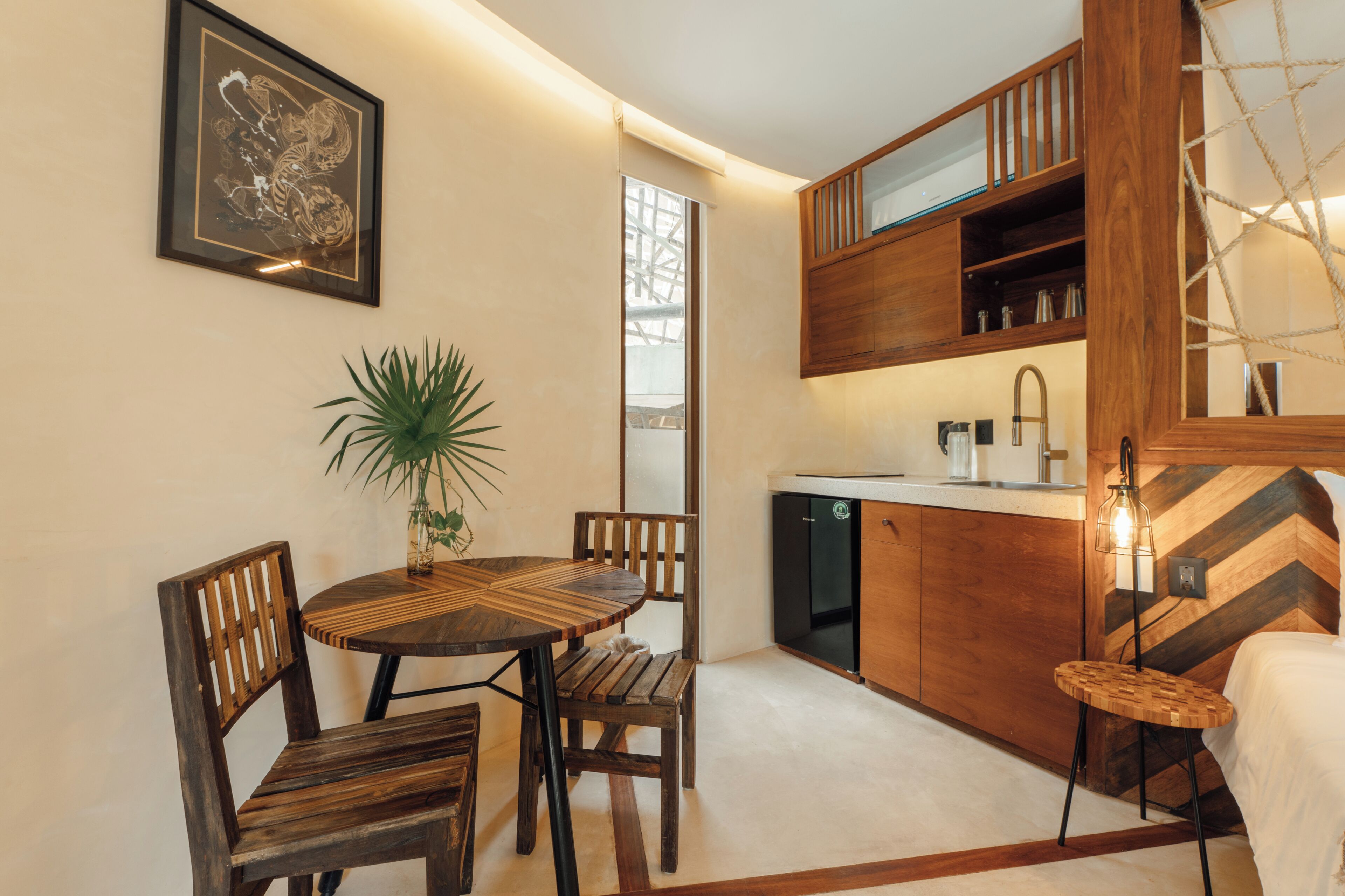A compact kitchen with wooden cabinets, a dining area with a round table and chairs, and a hanging light fixture.
