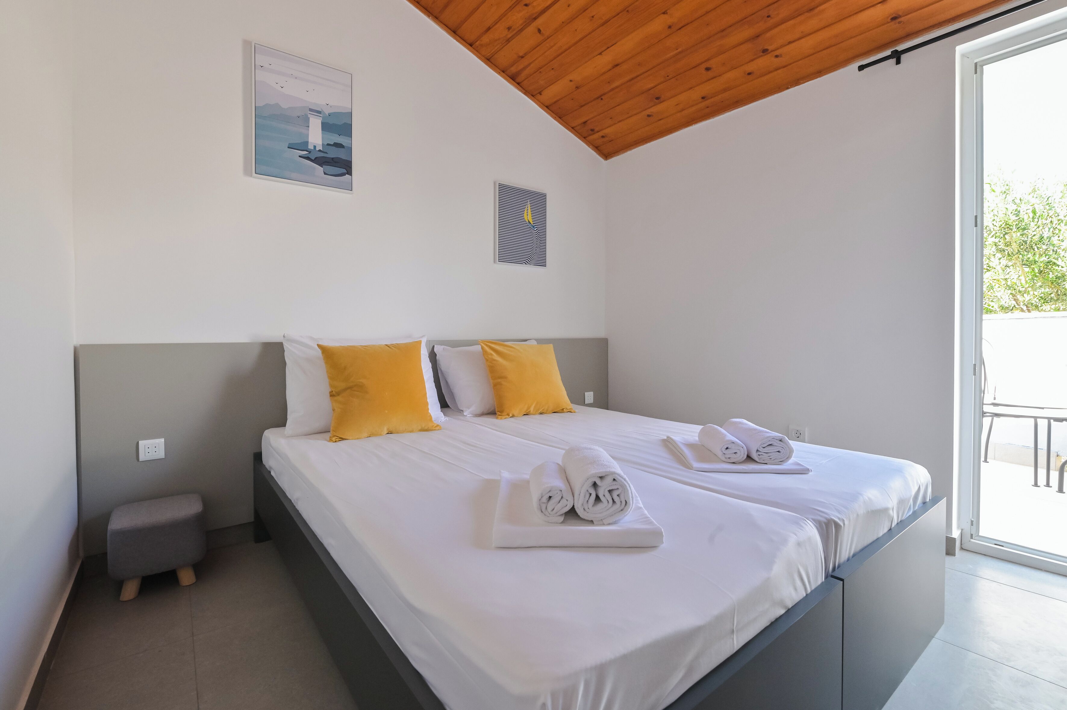 A bedroom with a bed, two pillows, a small stool, and a window.