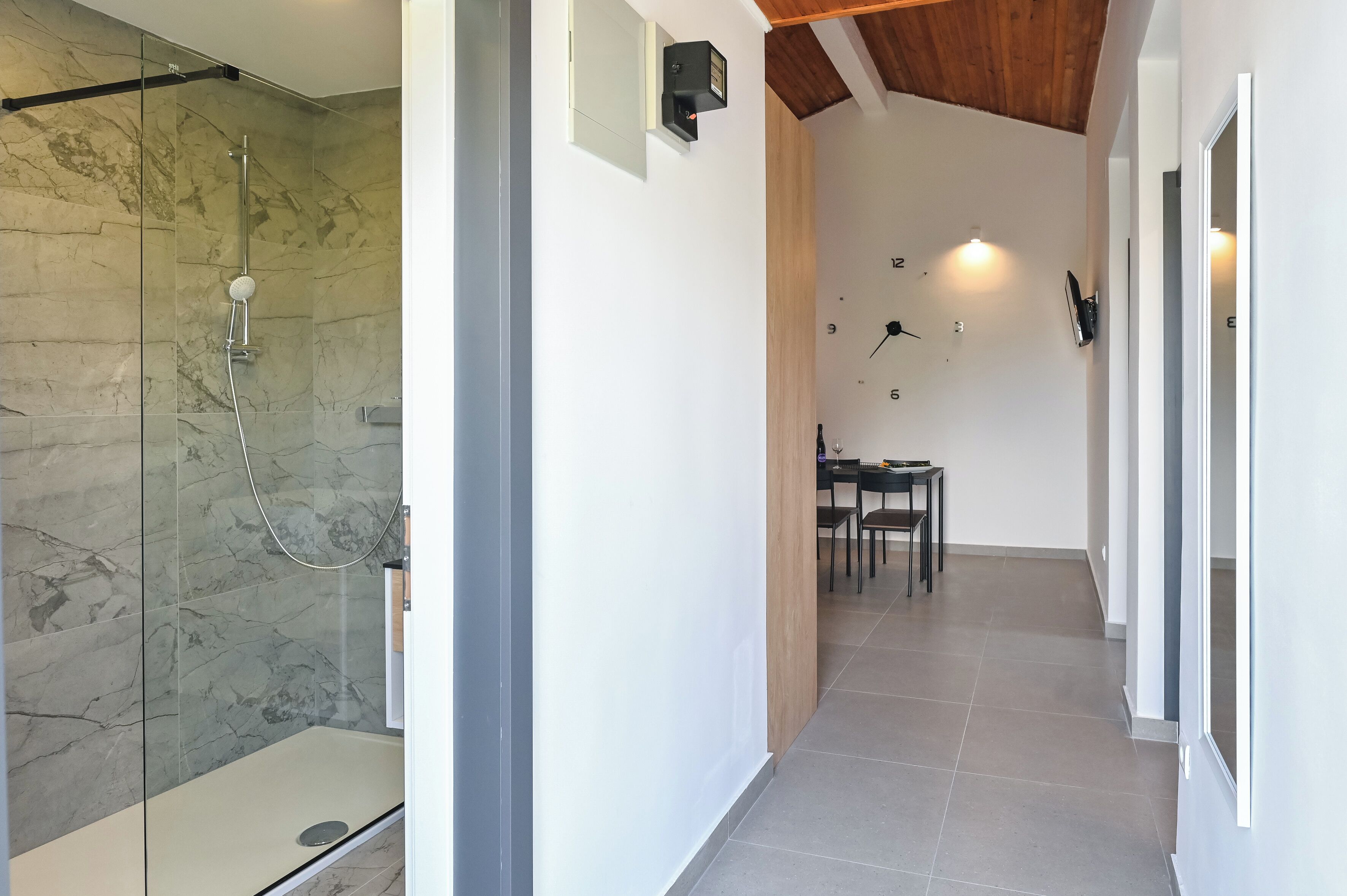 A modern bathroom with a glass-enclosed shower, a wooden ceiling, and a dining area with chairs and a table.