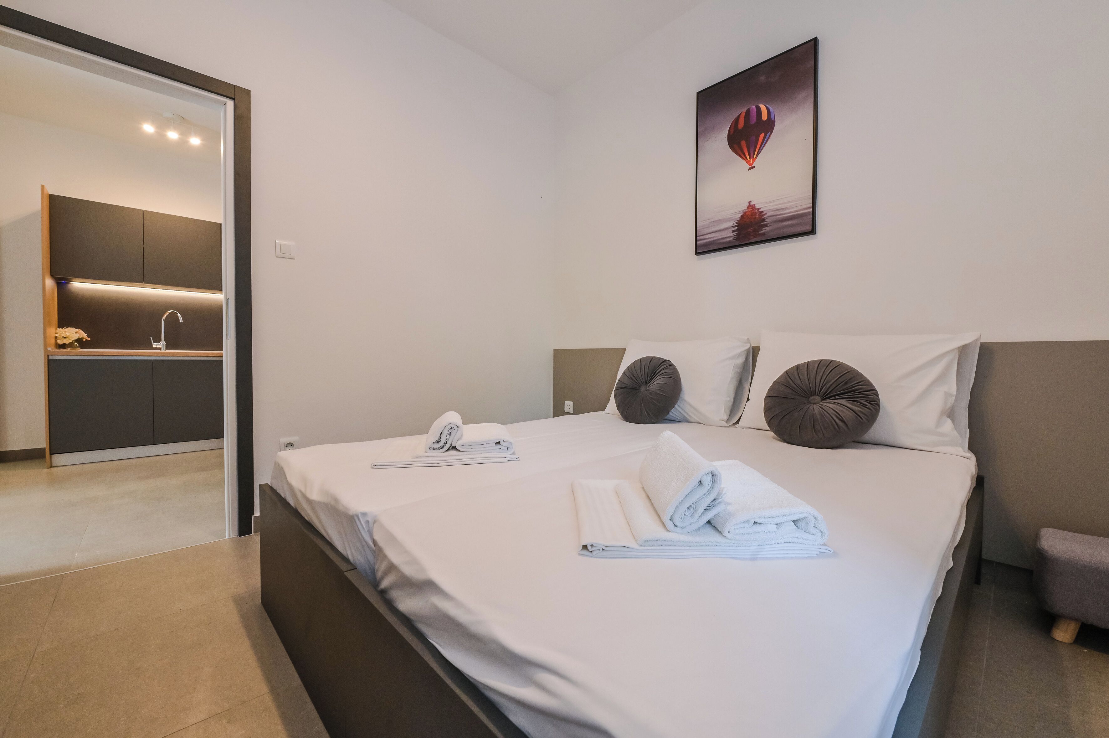 A modern hotel room with a large bed, two pillows, a bedside table, and a painting of a hot air balloon.