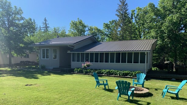 Ein Haus mit überdachter Veranda, Feuerstelle und Gartenmöbeln.