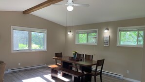Ein Essbereich mit Holztisch, Stühlen und Deckenventilator. Es gibt Fenster mit Jalousien, eine Wandleuchte und ein Schild an der Wand.