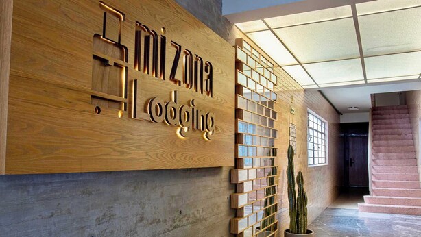 A wooden reception desk with the name "Mi Zona Lodging" and a glass partition with a potted plant. - Hidden gem near WTC | Bright & Chic (Ciudad de México)