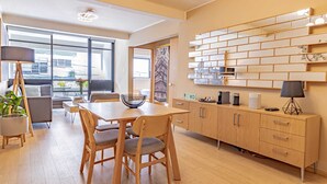 Une cuisine moderne avec des meubles en bois, une table à manger et des chaises. Une grande fenêtre laisse entrer la lumière naturelle et offre une vue sur l’extérieur.