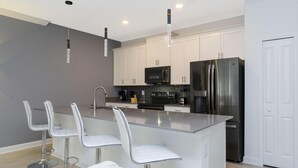 A modern kitchen with white cabinets, stainless steel appliances, and a central island with bar stools. - Brand New at Storey Lake Resort, Private Pool, Near Famous Attractions!! (Kissimmee)