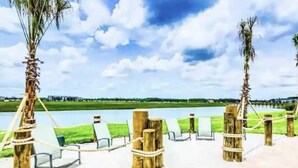 A beachside lounge with wooden posts and white ropes, overlooking a calm lake and green landscape. - Brand New at Storey Lake Resort, Private Pool, Near Famous Attractions!! (Kissimmee)