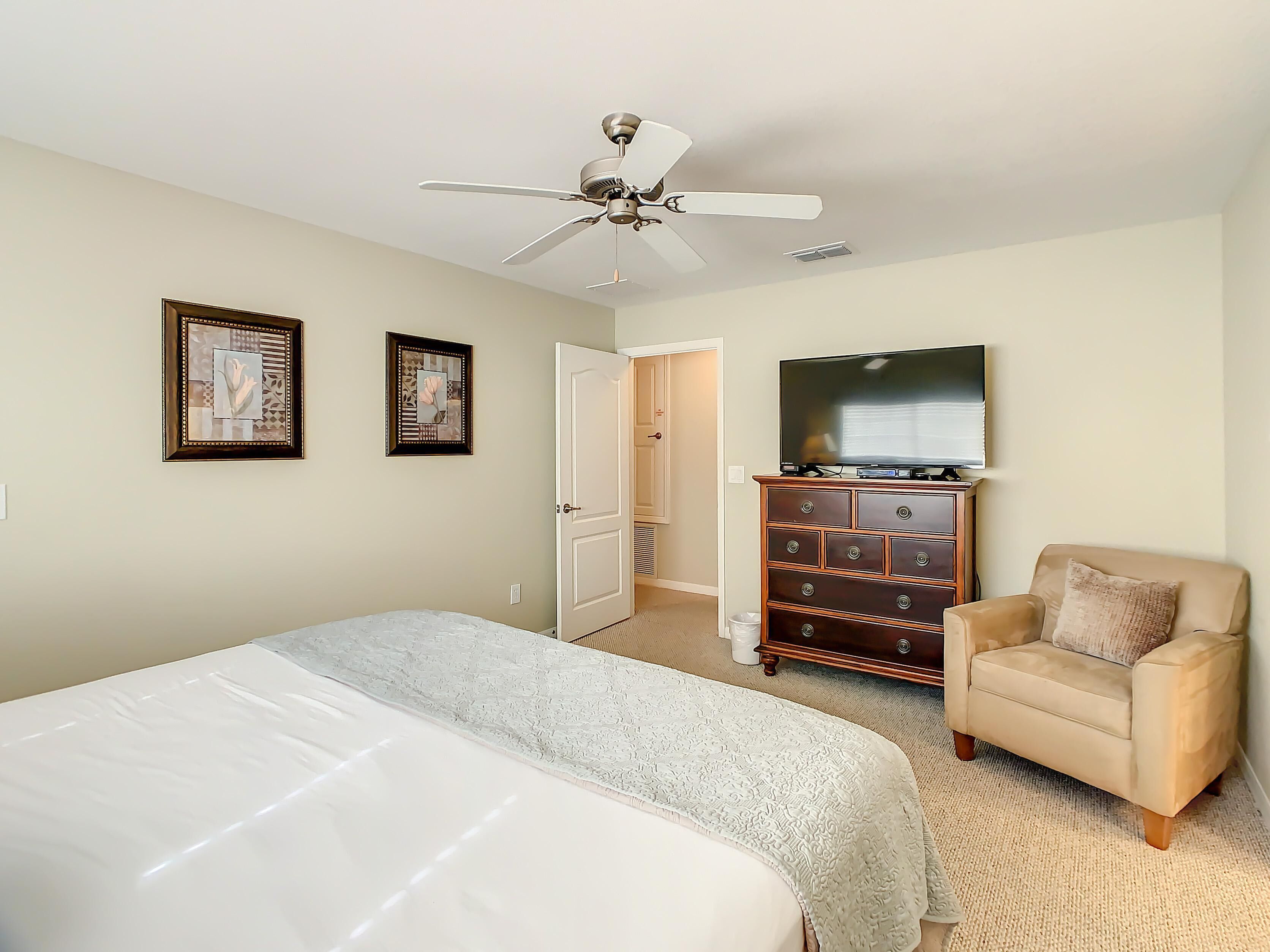 A bedroom with a bed, a chair, a dresser, a ceiling fan, and a TV.