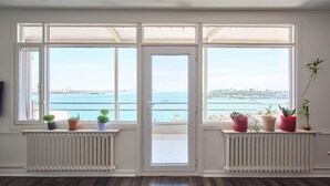 A room with a large bay window overlooking a coastal view, featuring a radiator, a television, and several potted plants. - A MILLION DOLLAR VIEW IN THE HEART OF ISTANBUL (İstanbul)