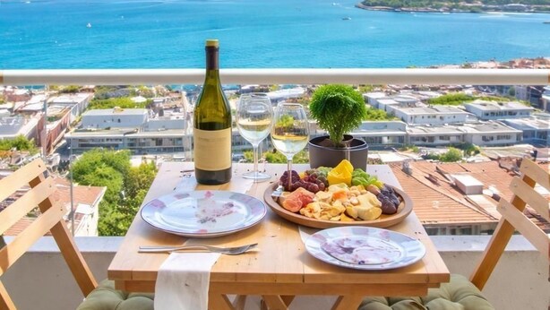 A table with a bottle of wine, glasses, and a fruit platter on a balcony overlooking a coastal city. - A MILLION DOLLAR VIEW IN THE HEART OF ISTANBUL (İstanbul)