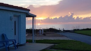 Un edificio con un portico coperto, due sedie di plastica blu e vista sul tramonto sull'acqua.