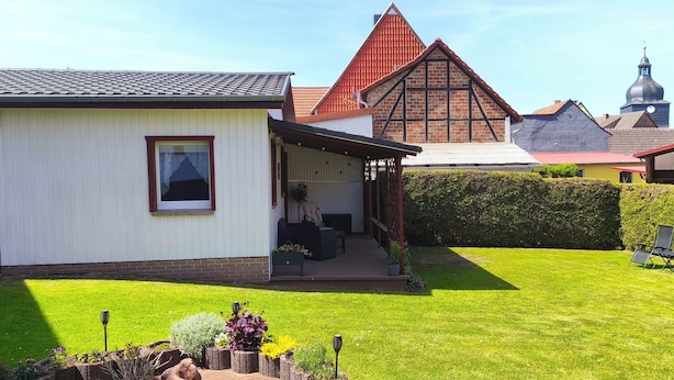 Ein Haus mit überdachter Veranda, einem gepflegten Rasen und einem Nachbargebäude mit auffälligem roten Dach.