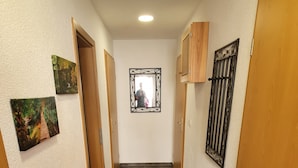 Ein Korridor mit dunklen Fliesen, Holztüren und einem Spiegel an der Wand.
