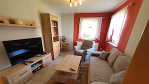 Ein modernes Wohnzimmer mit Flachbildfernseher, Holzmöbeln, einer Couch und einem dekorativen Teppich.