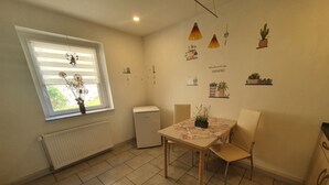 Eine kompakte Küche mit Fenster, einem kleinen Kühlschrank, einem Tisch mit Stühlen und an der Wand befestigten Pflanzen.