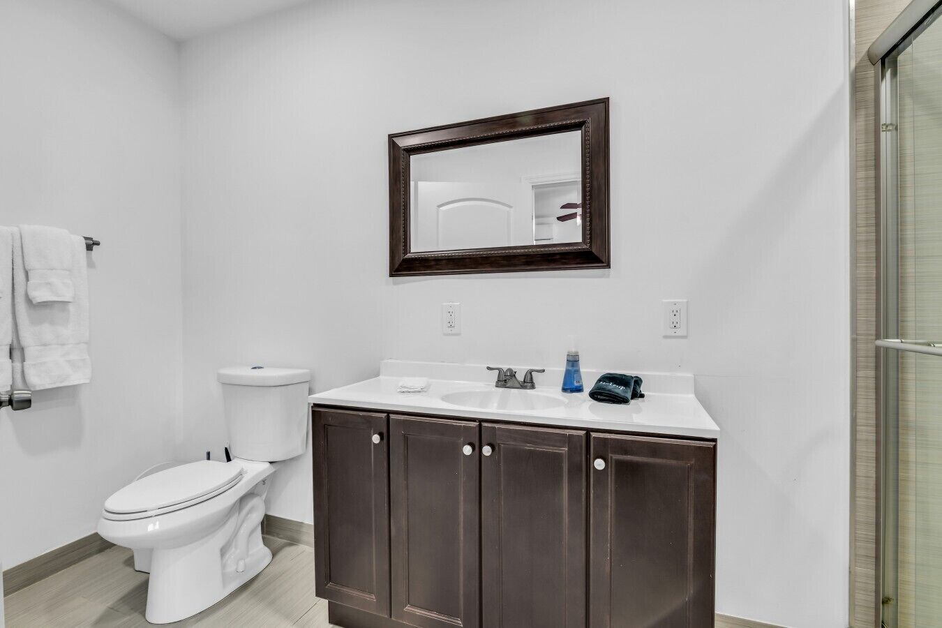 A bathroom with a white toilet, a dark wooden vanity, a white sink, and a mirror above the vanity.
