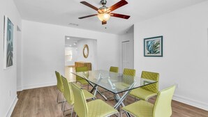 A modern dining area with a glass table and green chairs, a ceiling fan, and a framed picture on the wall.