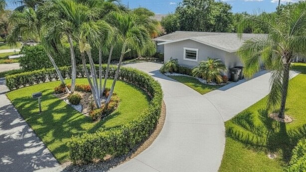 A single-story house with a curved driveway, surrounded by well-maintained landscaping and palm trees.