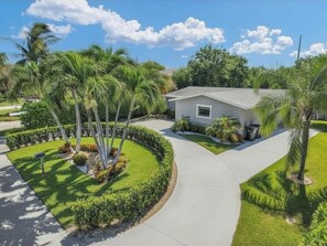 A single-story house with a curved driveway, surrounded by well-maintained landscaping and palm trees.