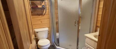 A compact bathroom with a shower, toilet, and sink, featuring wooden walls and a patterned rug.