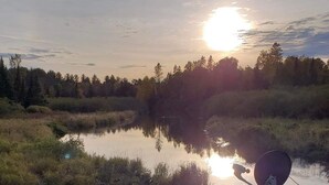 A calm river with a sunset in the background and a satellite dish in the foreground.