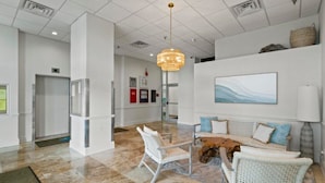 A lobby with a white reception desk, a seating area with wicker furniture, a large abstract painting, and a hanging light fixture.