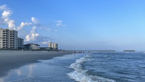 A beach with a pier extending into the ocean, buildings in the background, and waves gently lapping at the shore. - Oceanfront Holiday Getaway (North Myrtle Beach)