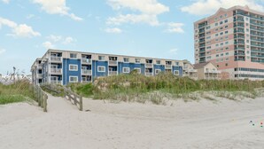 A beachfront building with multiple balconies, a wooden walkway, and a sandy beach. - Oceanfront Holiday Getaway (North Myrtle Beach)