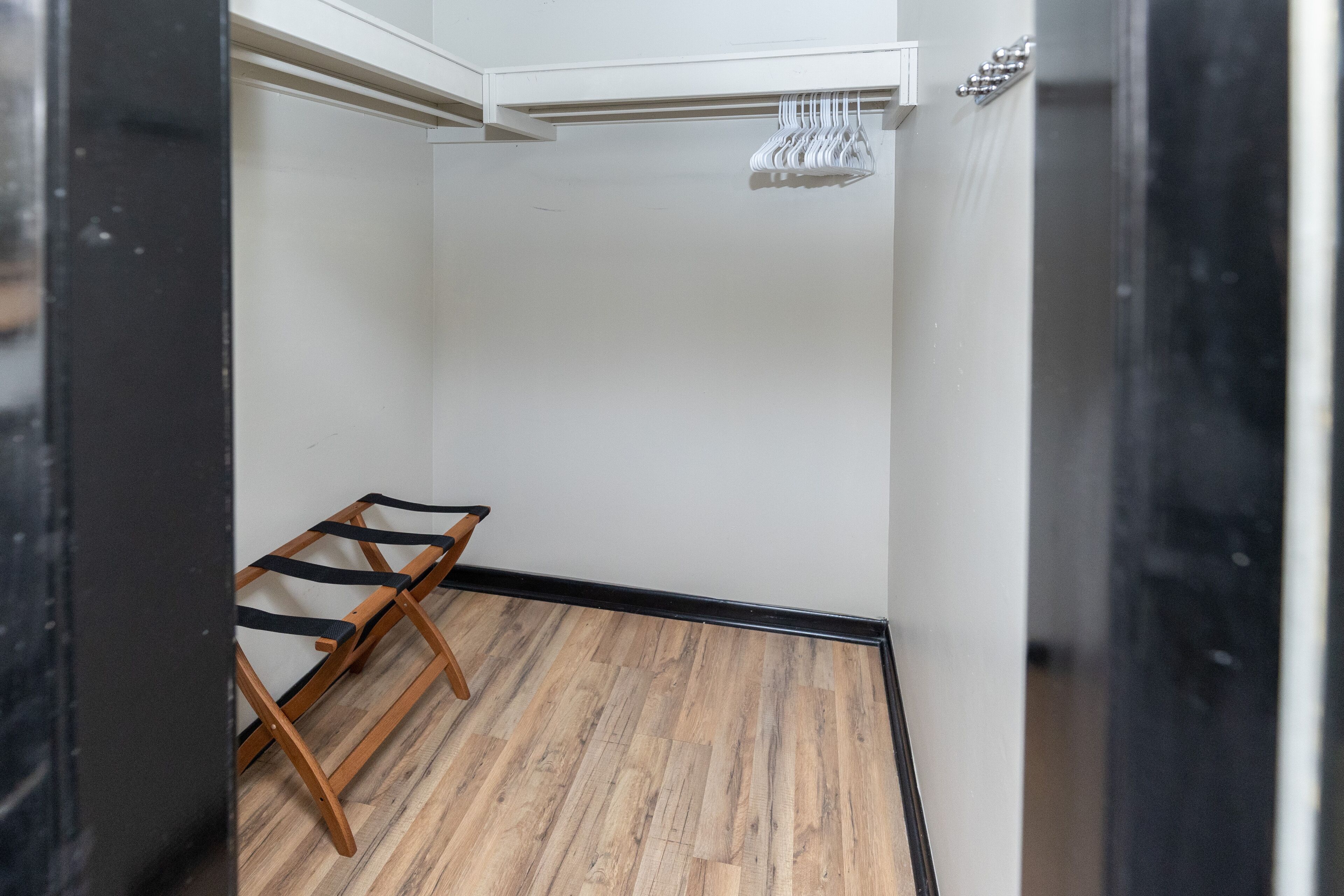 A small, empty room with wooden flooring, a metal rack, and a white ceiling.