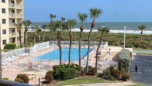 A pool area with palm trees and a view of the ocean. - Beachfront (Cape Canaveral)