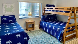 A room with two bunk beds, a small table with a lamp, a window with vertical blinds, and a ceiling fan. - Beachfront (Cape Canaveral)